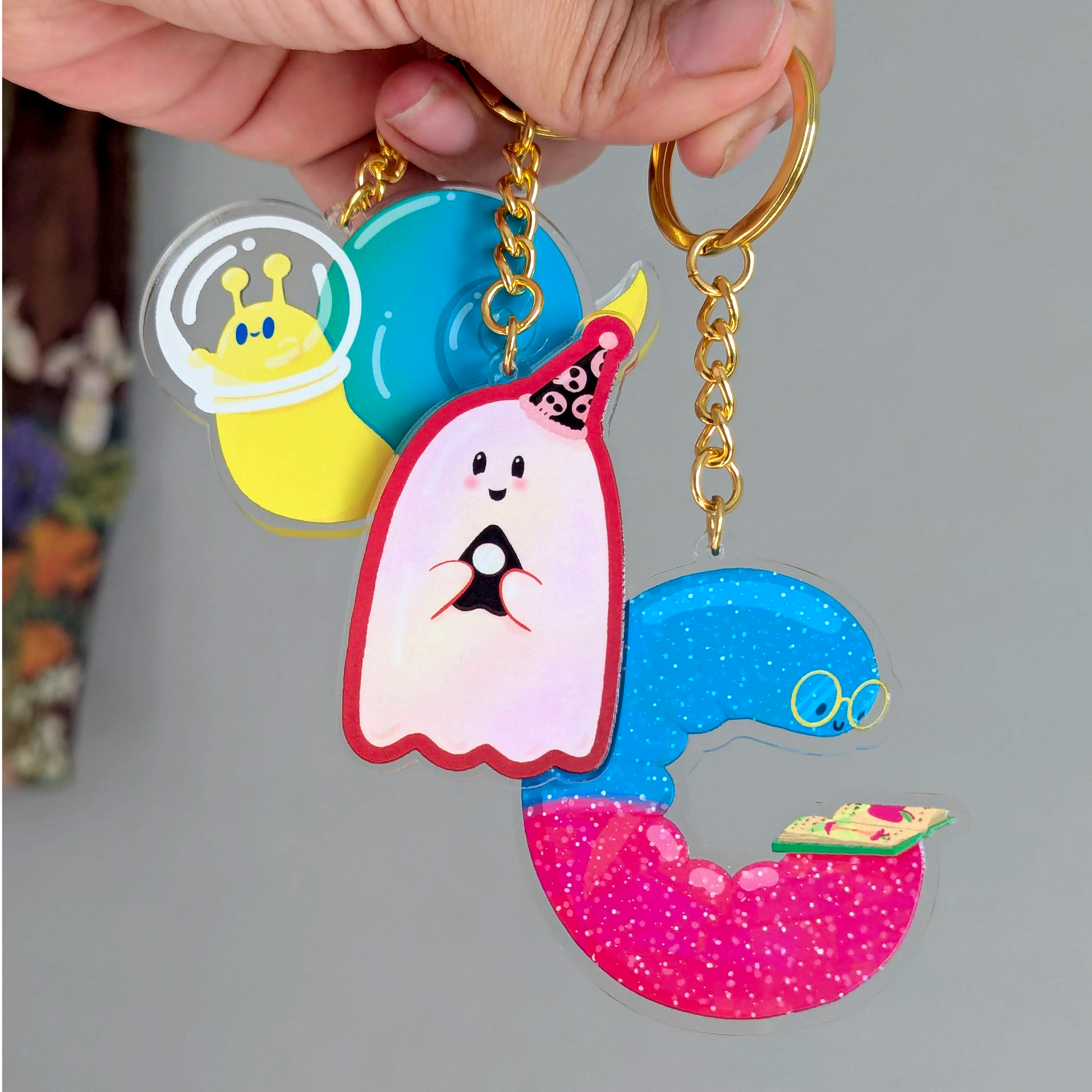 Colorful cartoon character keychain held by a hand on a gray background